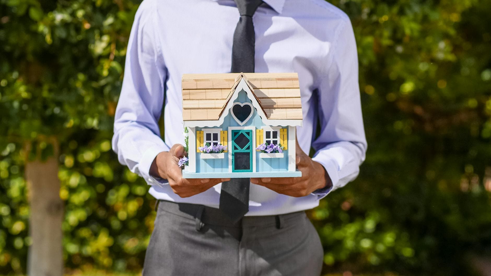 A business professional holds a decorative miniature house, symbolizing real estate investment.